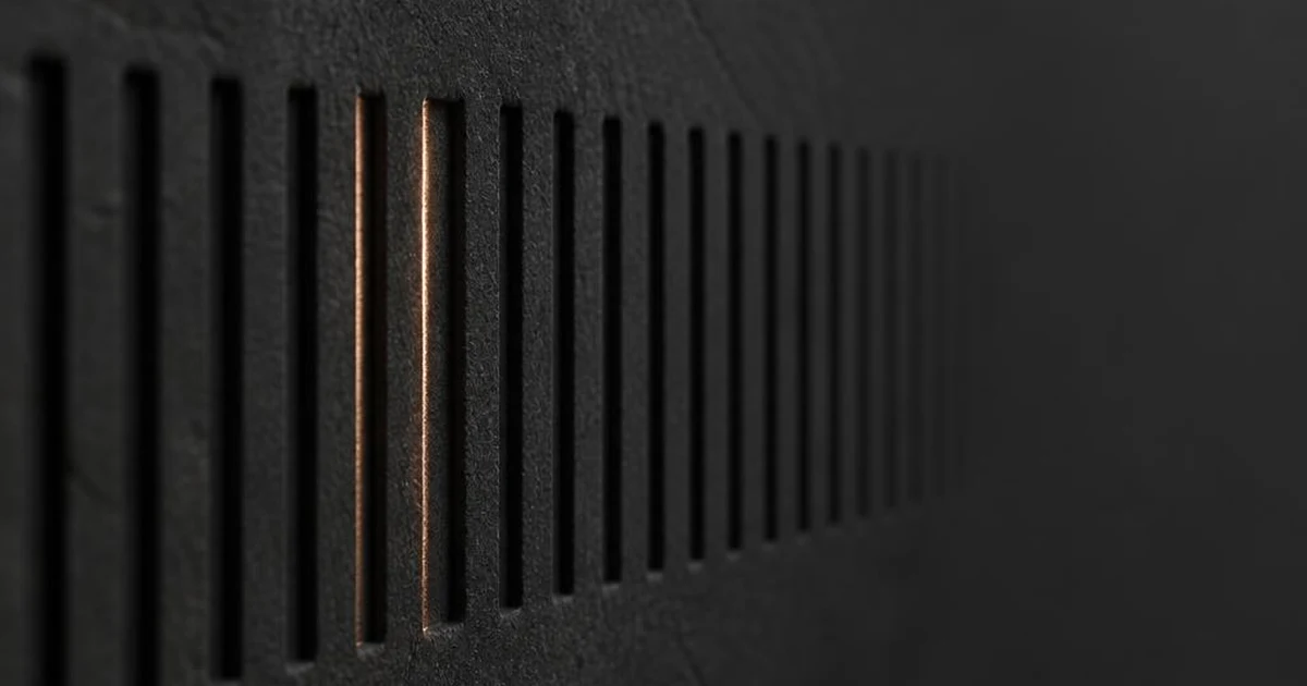Row of narrow machined grooves cut into a dark charcoal surface, two of them lit by a warm copper highlight, standing for picking one version out of many