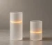 Two frosted glass cylinders of different heights standing on a stone surface, each circled by a glowing amber light ring at a different height